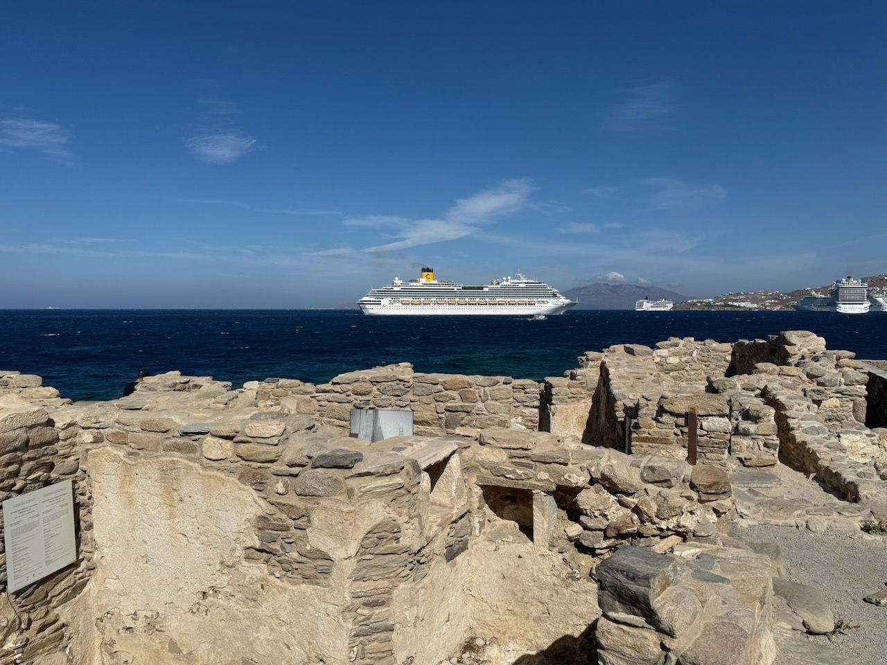 In the foreground a jumble of stone walls, the ruins of buildings. There's a big cruise ship in the distance.