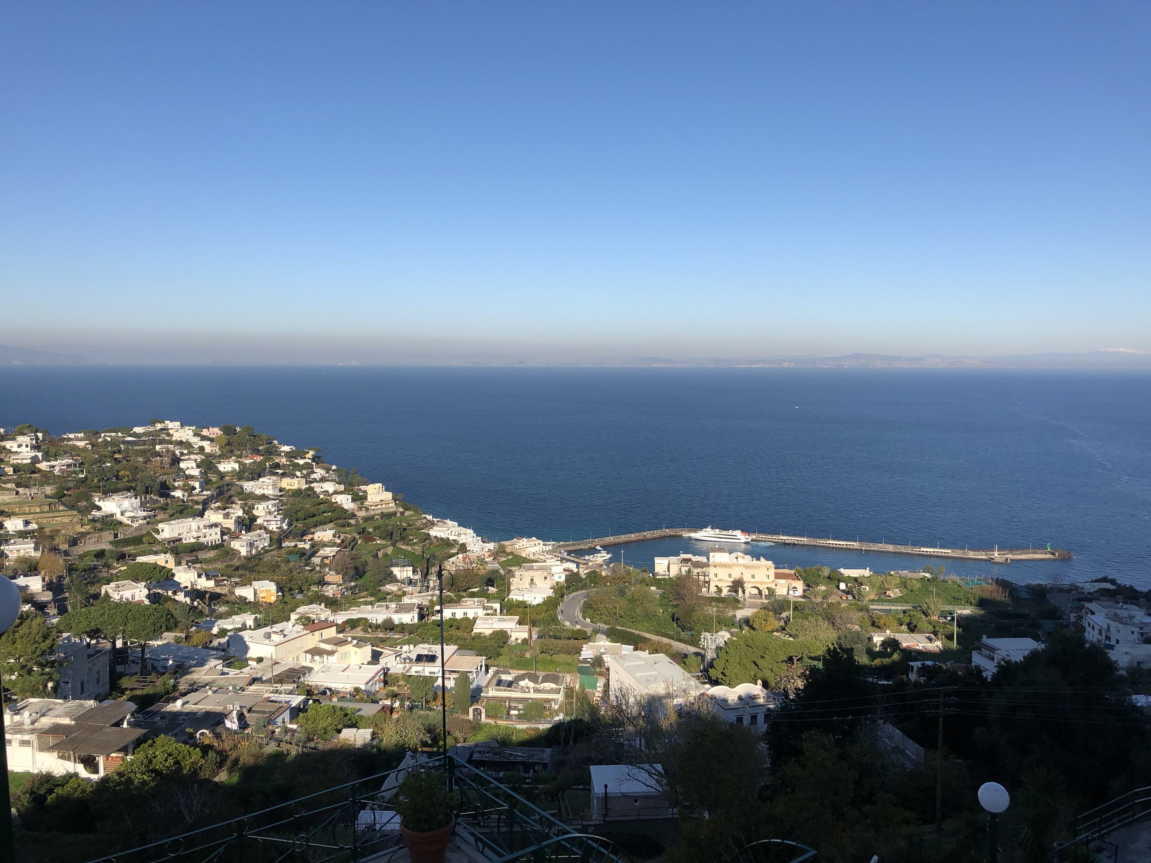 Elevated view of Marina Grande and the surrounding town of Capri, with a pier extending into the deep blue sea.