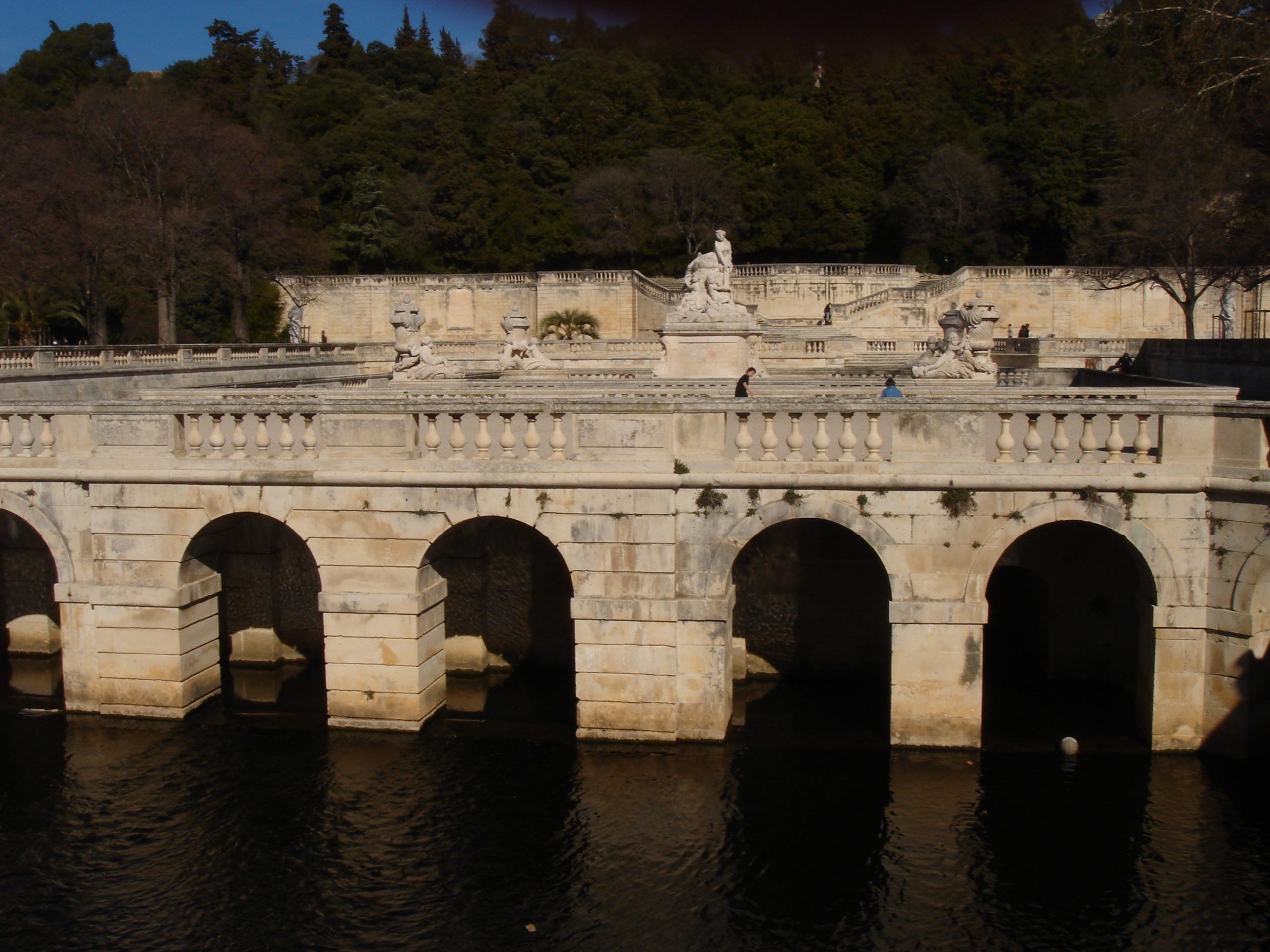 View of the fountain and sculptures above the arched water channel in the Jardins de la Fontaine.