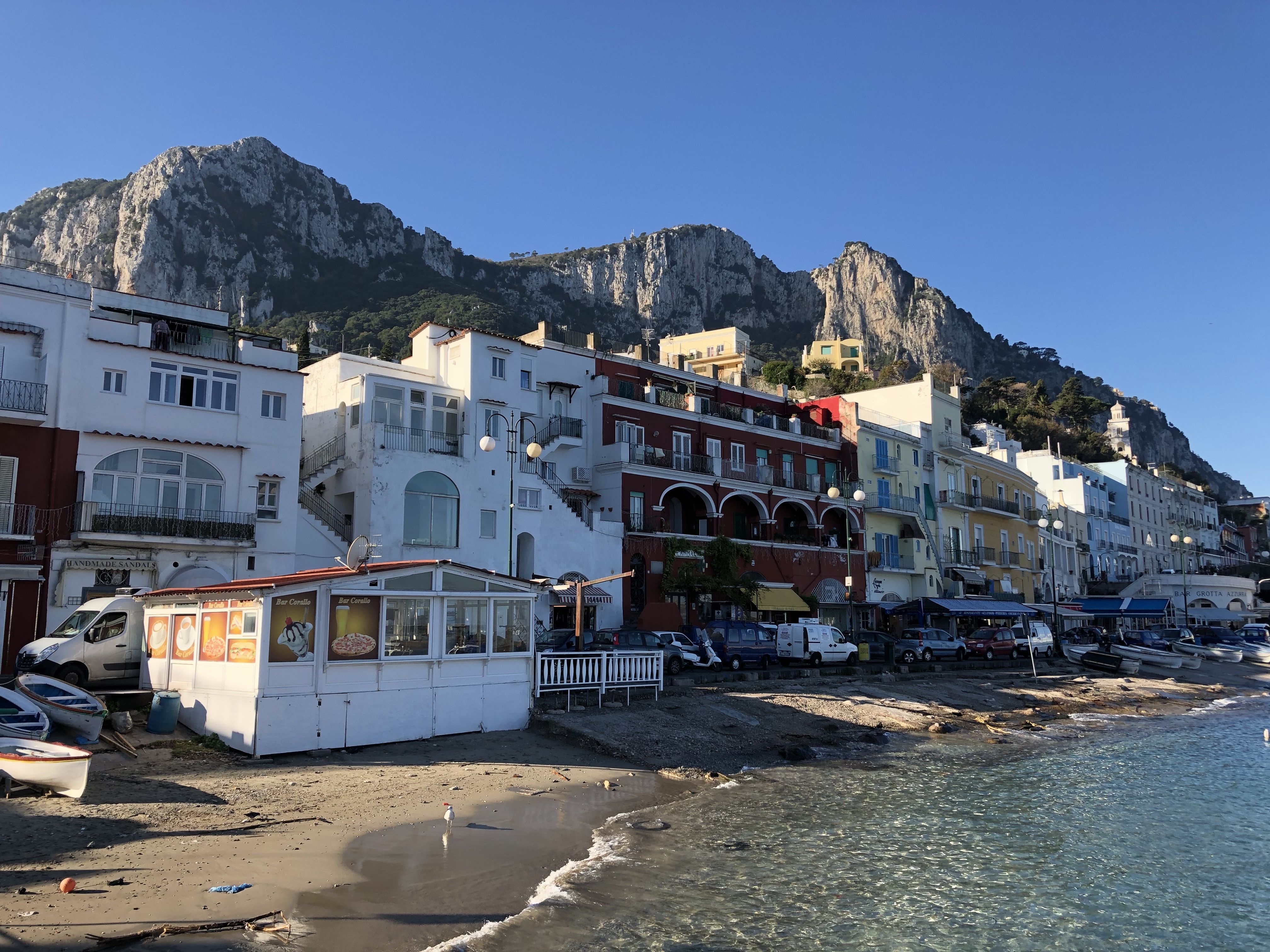 View along the shoreline at Capri, with pastel buildings and restaurants facing the calm sea under rugged limestone cliffs.
