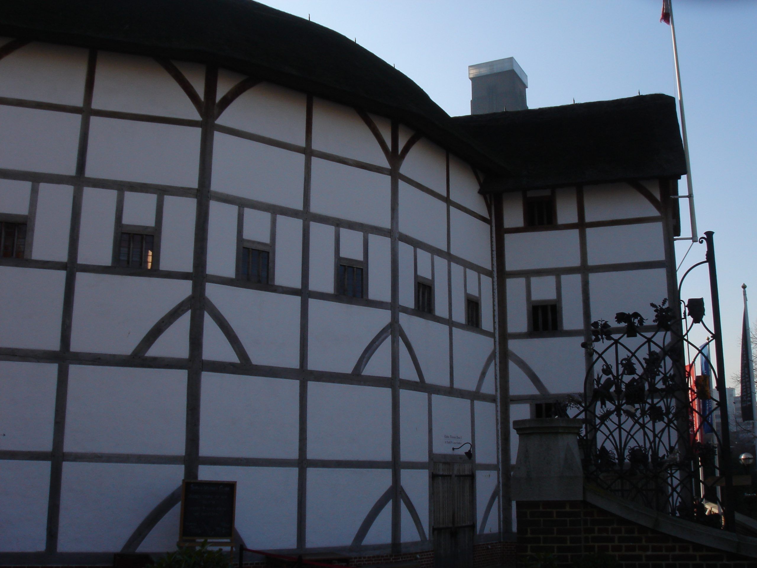 Side view of Shakespeare's Globe Theatre in London, featuring its white and wooden panel exterior with small windows and a thatched roof.
