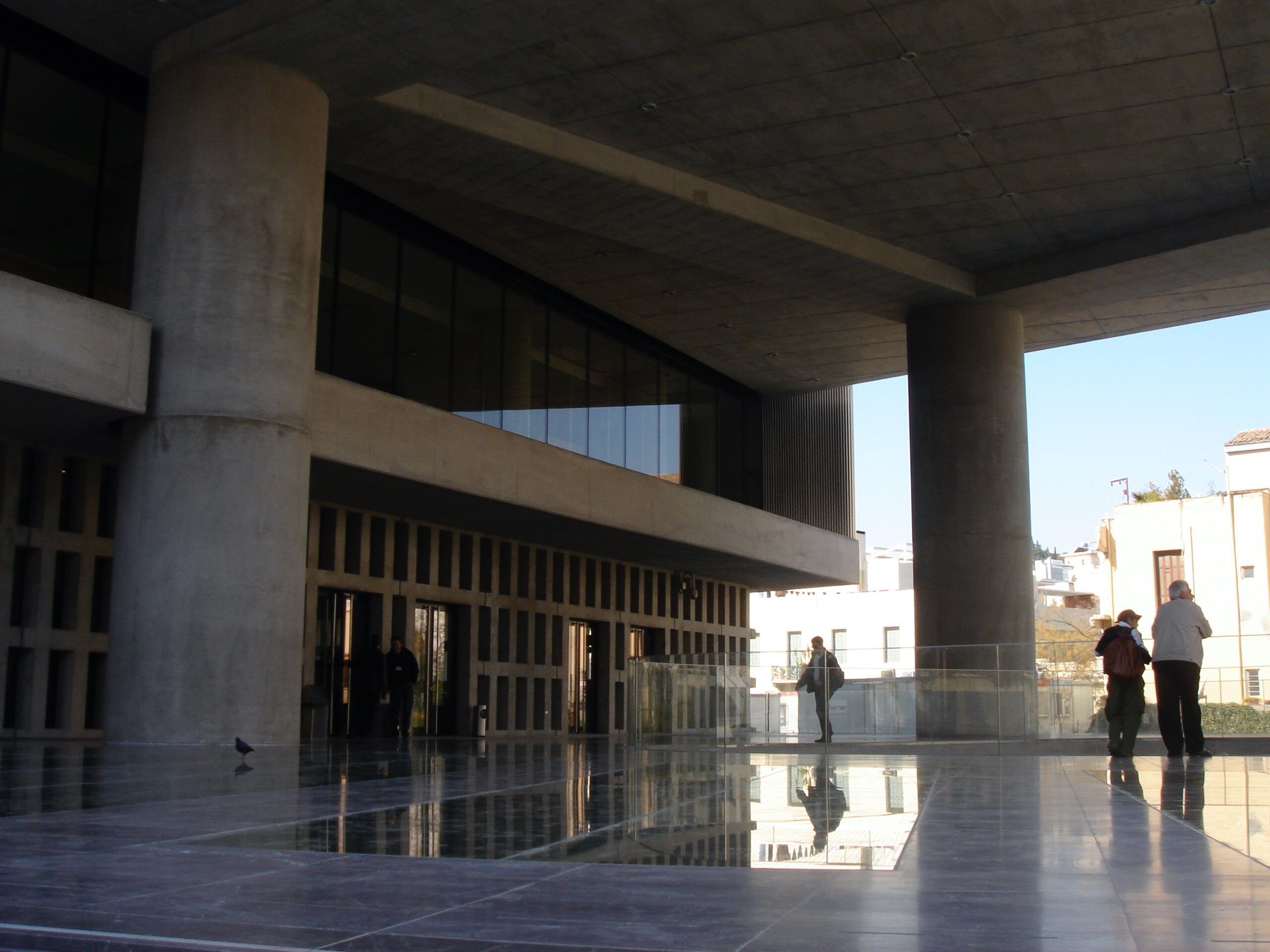 Modern architecture of the New Acropolis Museum in Athens, with broad concrete columns and a reflective glass floor.