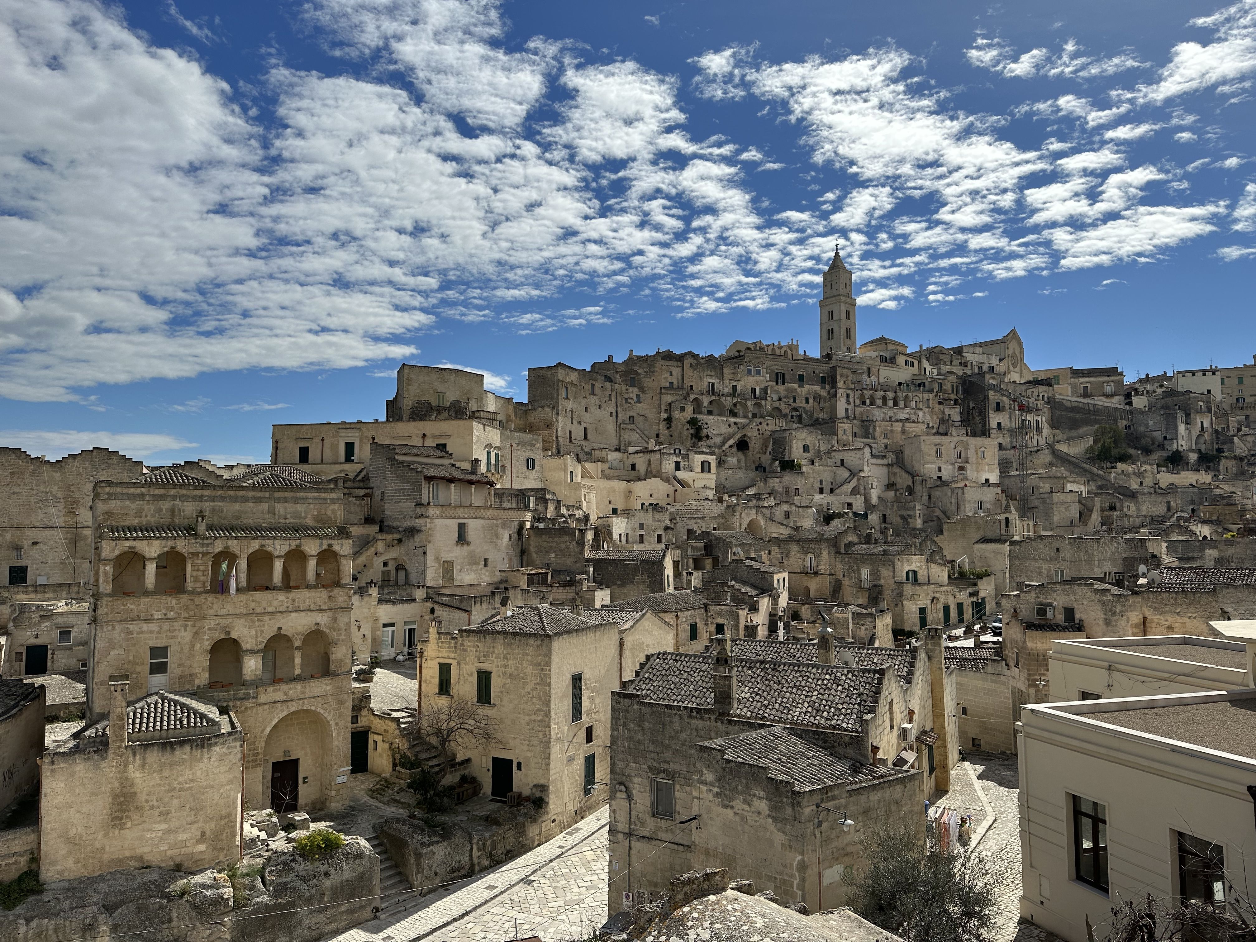 Panoramic view of the Sassi in Matera under a bright blue sky, with pale stone houses and the cathedral rising on the hill.
