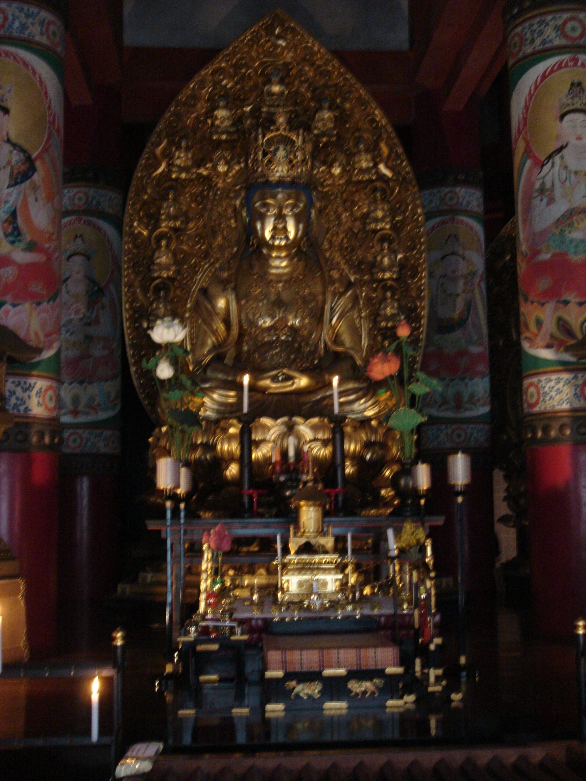 An ornate golden Buddha statue surrounded by offerings and candlelight inside a temple.