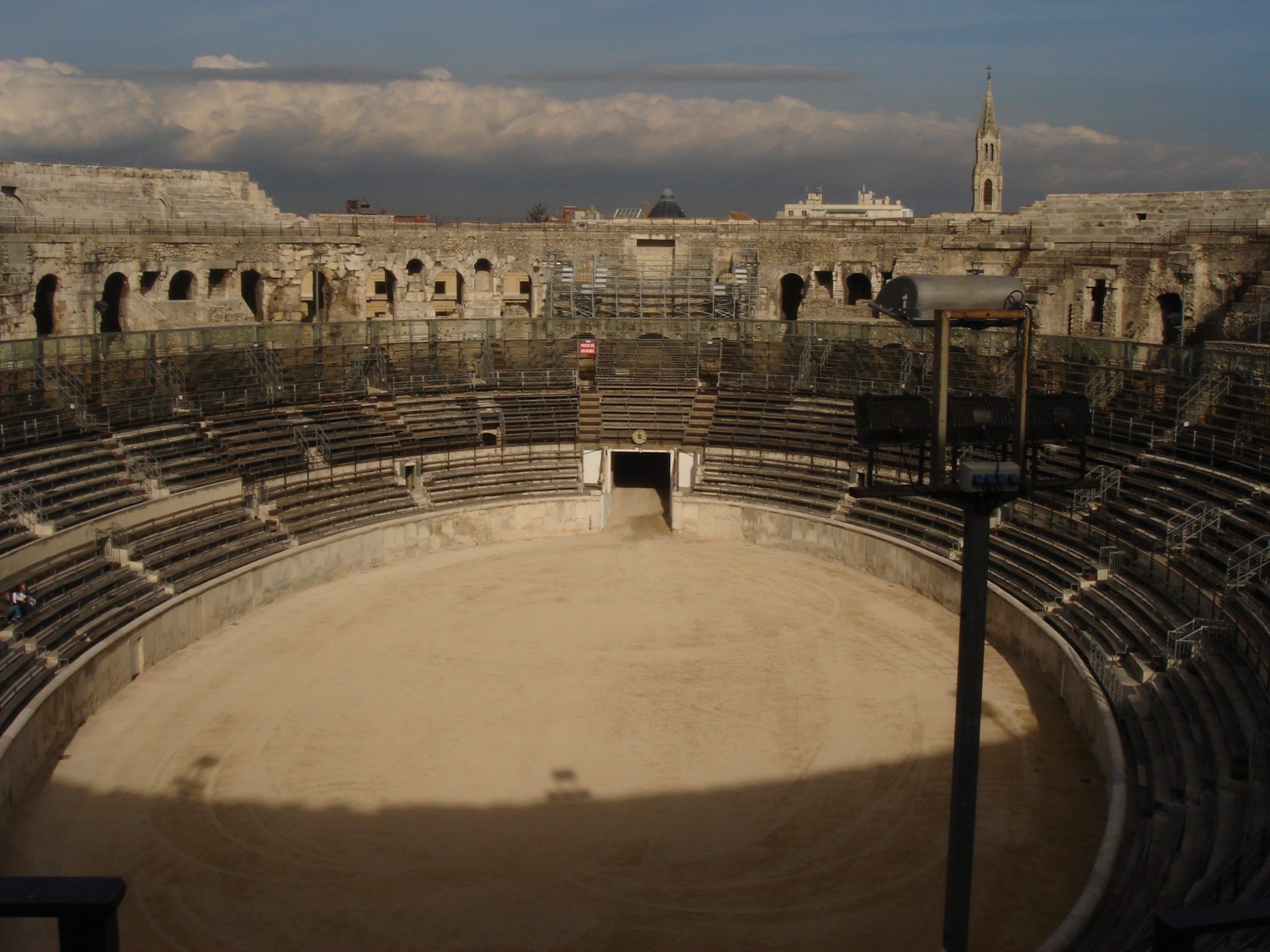 Wide view of the Roman amphitheatre in Nîmes from the seating tiers, showing the central arena, surrounding stands, and skyline beyond.