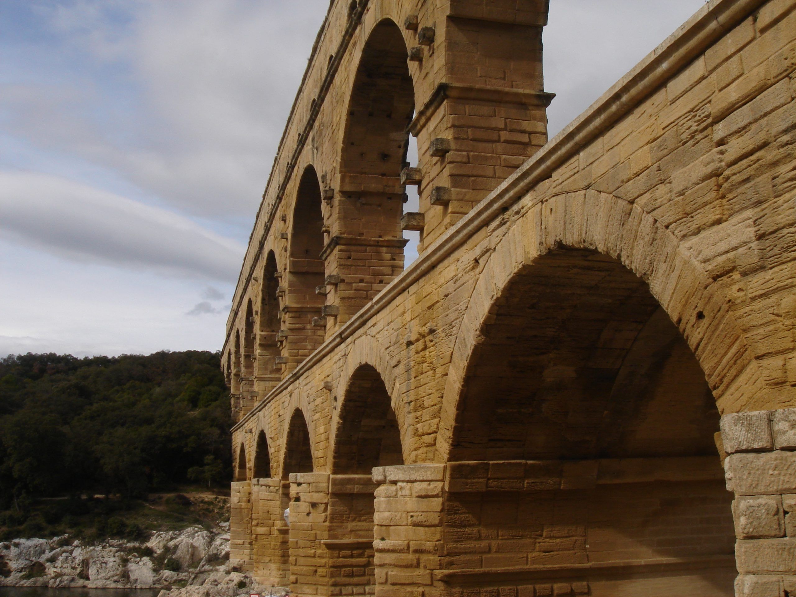 Low-angle view of the Pont du Gard from the riverbank, showing its massive stone arches and layered masonry.