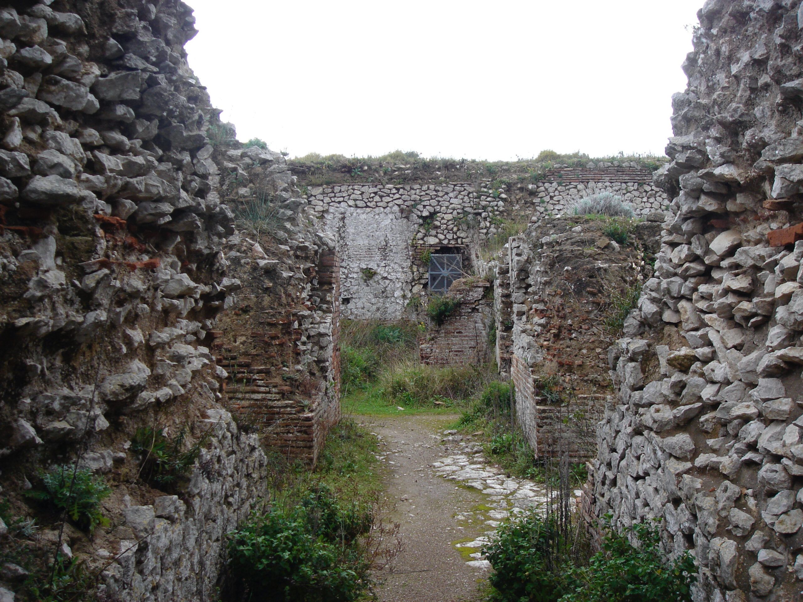 Ancient stone walls and ruins, partly overgrown with grass and weeds, seen from within the Villa Jovis on Capri.