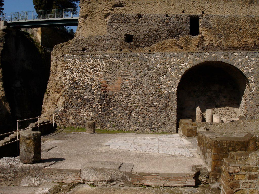 Paved platform and arched storage area at the seafront end of Herculaneum, backed by a high retaining wall of mixed stone and brickwork.