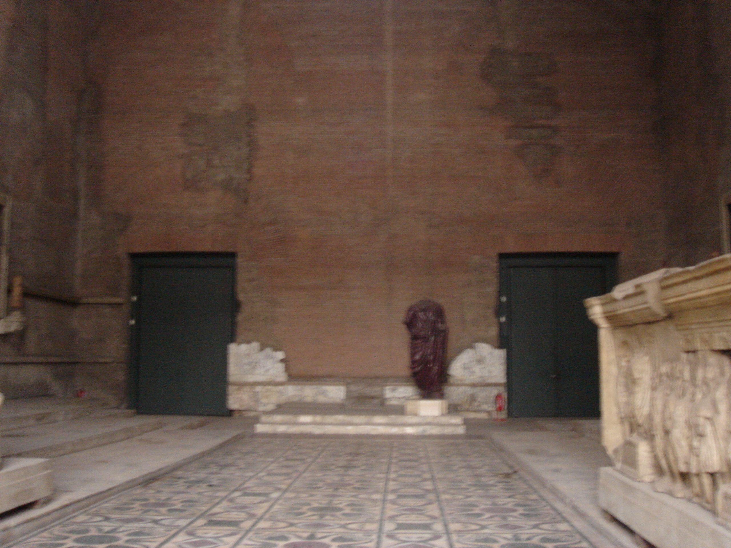 Interior of the Curia Julia with geometric patterned marble floor, a porphyry statue torso, and fragments of ancient sculptures.