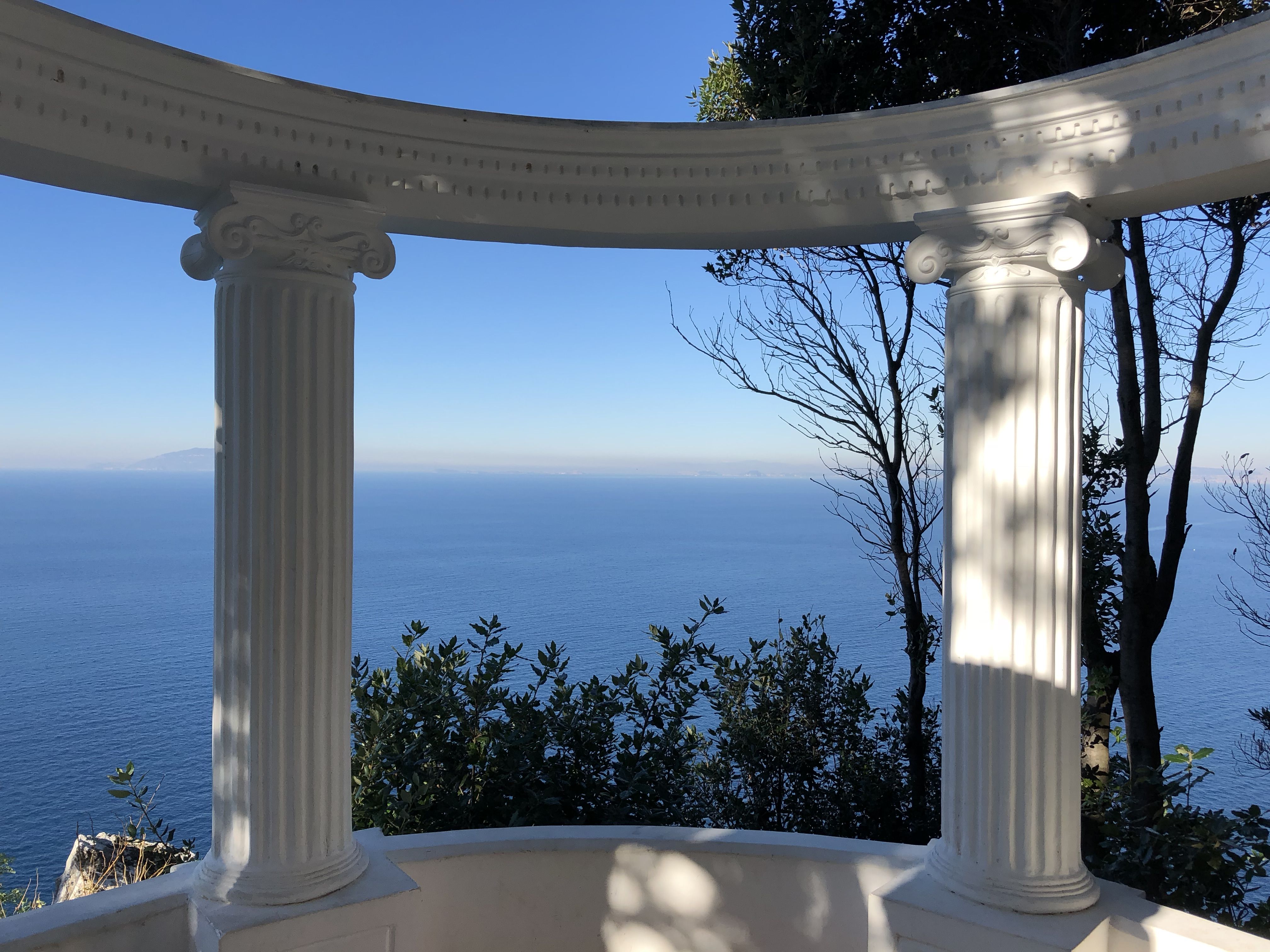 View of the blue sea framed by two white neoclassical columns on a circular terrace at Villa Lysis.