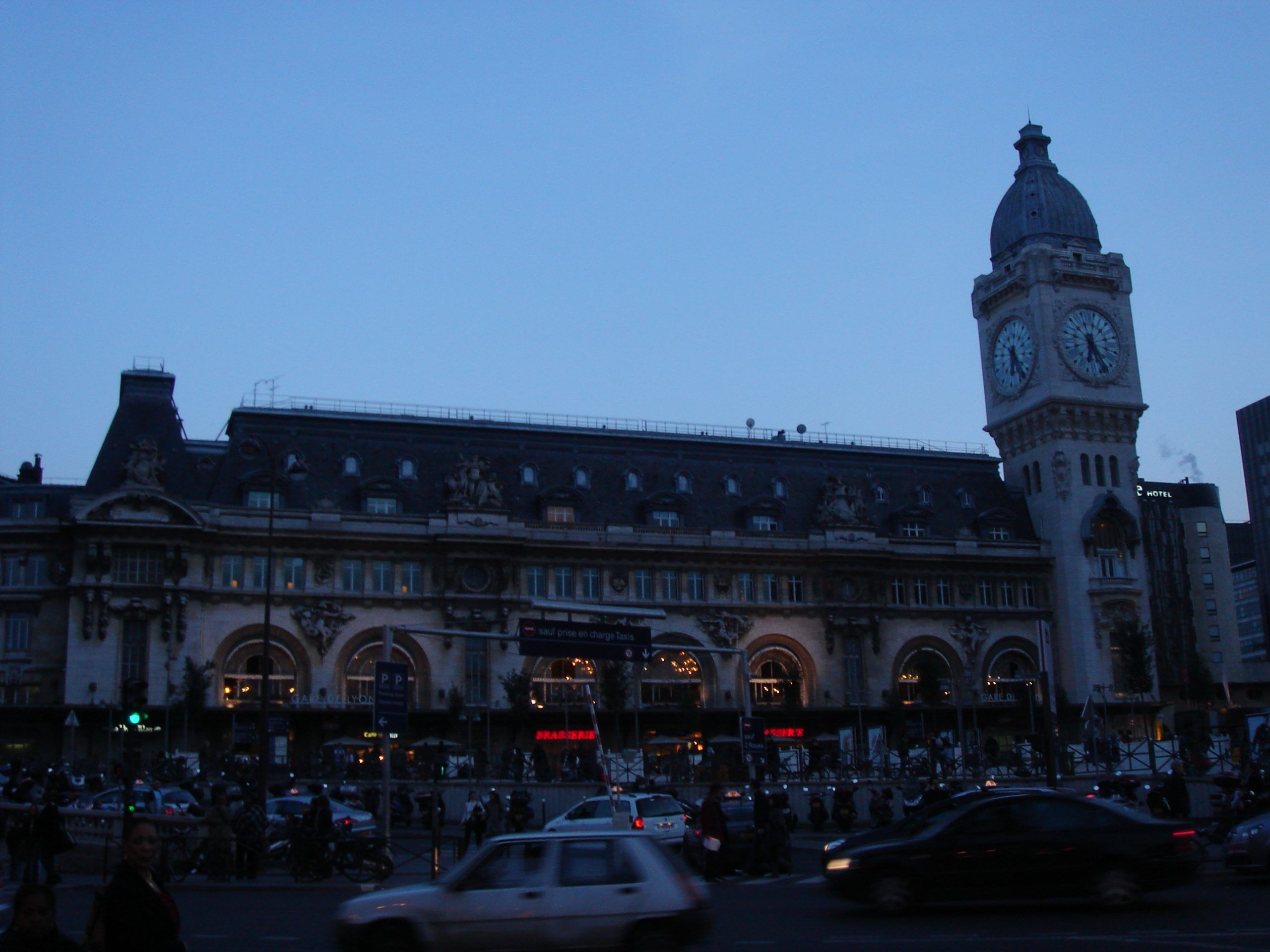Gare de Lyon in Paris at dusk with its clock tower and busy street in front.