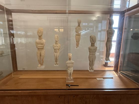 A glass cabinet containing six stylised female figurines of various sizes made out of white stone.