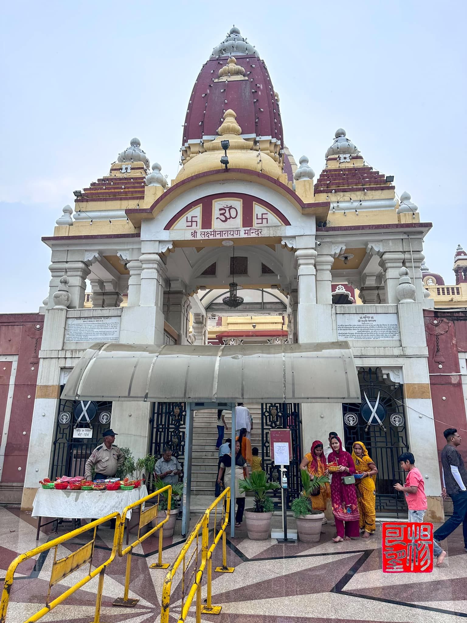 Entrance to the Shri Laxminarayan Temple in Delhi, with women in colorful sarees gathered near the gate and security guards on duty.