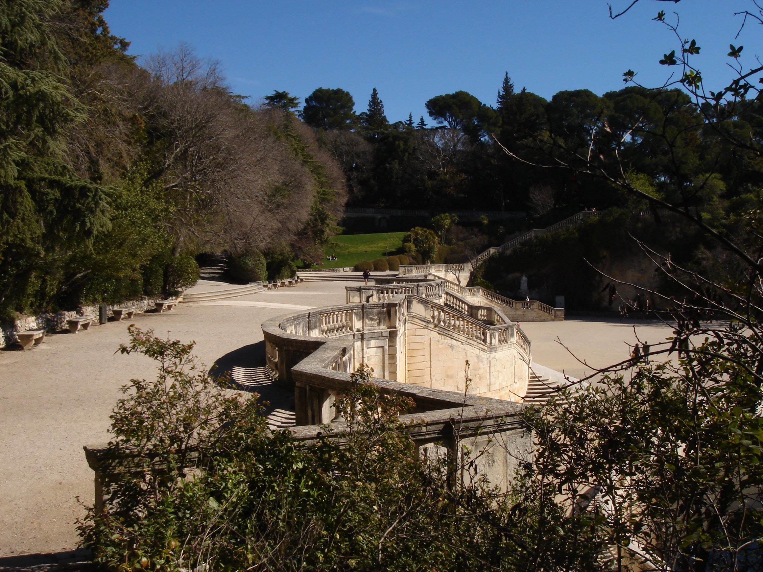 A grand stone staircase flanked by gardens and trees, in a formal park setting.