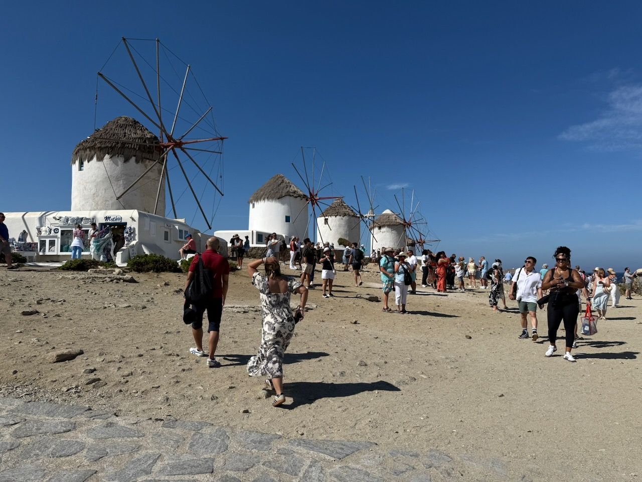 A row of cylindrical windmills. There are tourists all around. The sky is a deep blue.