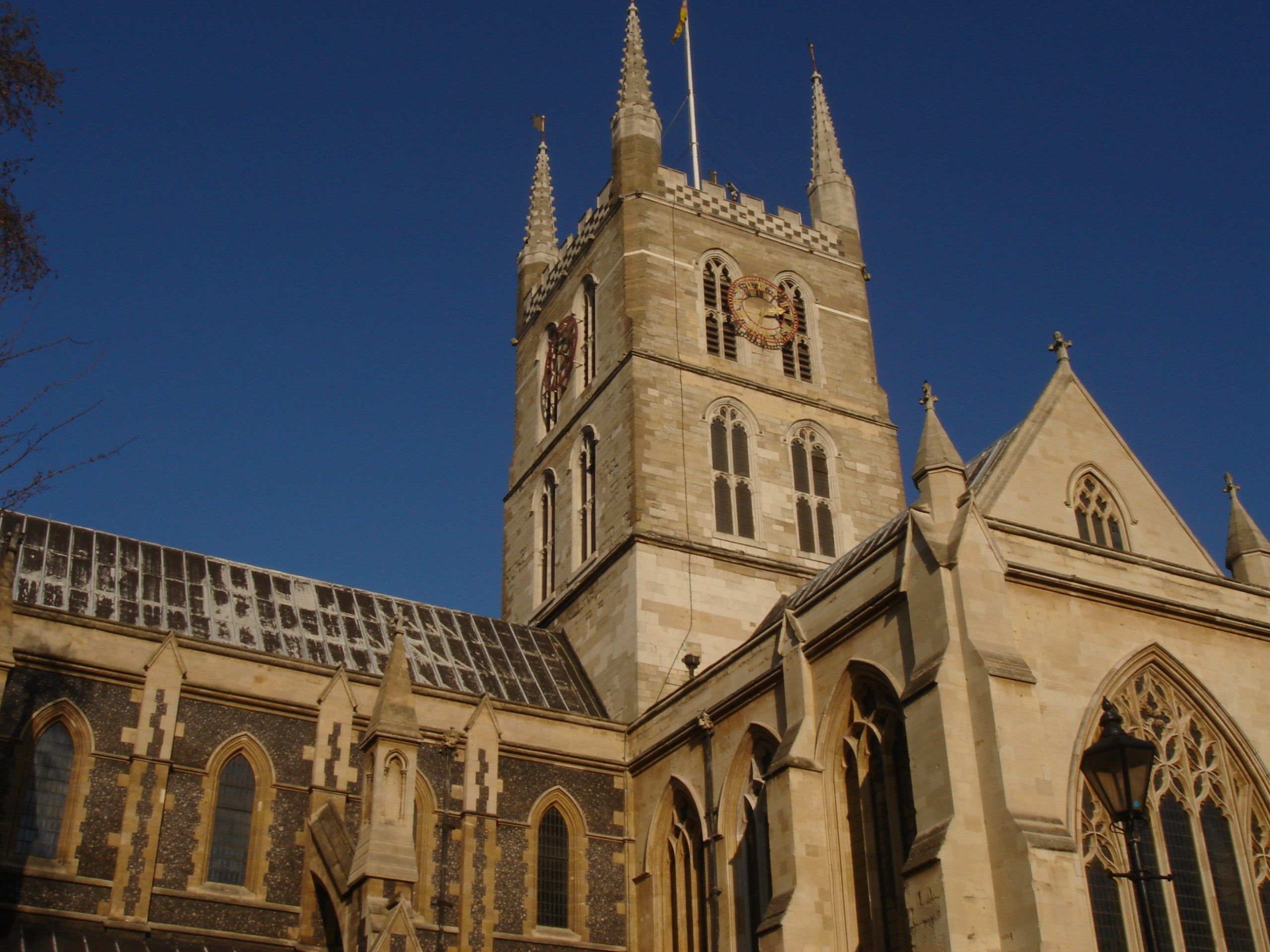 Southwark cathedral. Its sandstone is gold with sunlight and behind it the sky is a deep cloudless blue.
