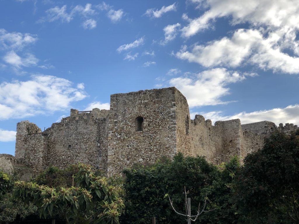 Looking at the outside of the castle. It's made of small yellow bricks of different sizes. On one corner is a square defensive tower.