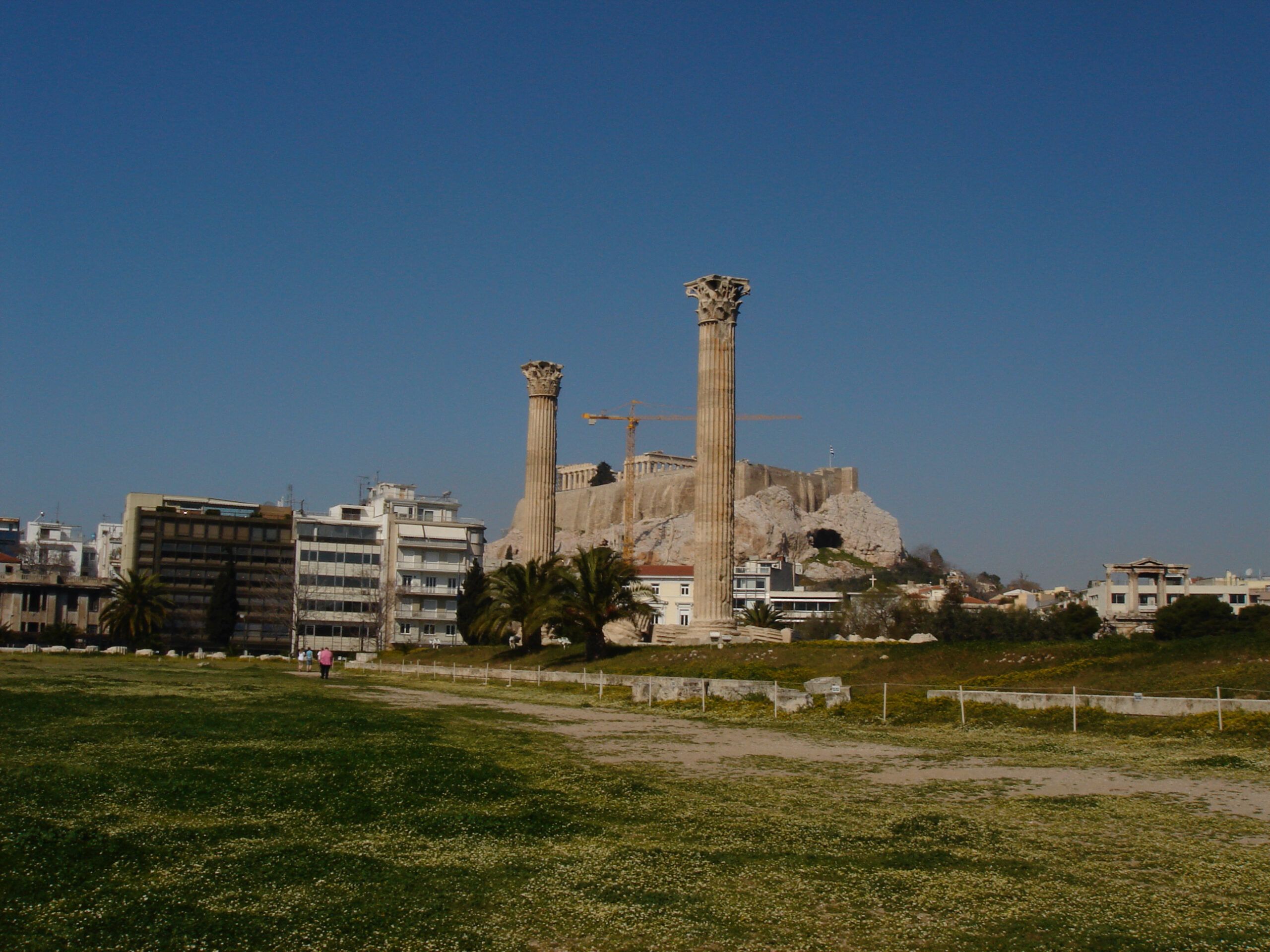 Two towering Corinthian columns from the Temple of Olympian Zeus with the Acropolis and modern Athens buildings in the background.