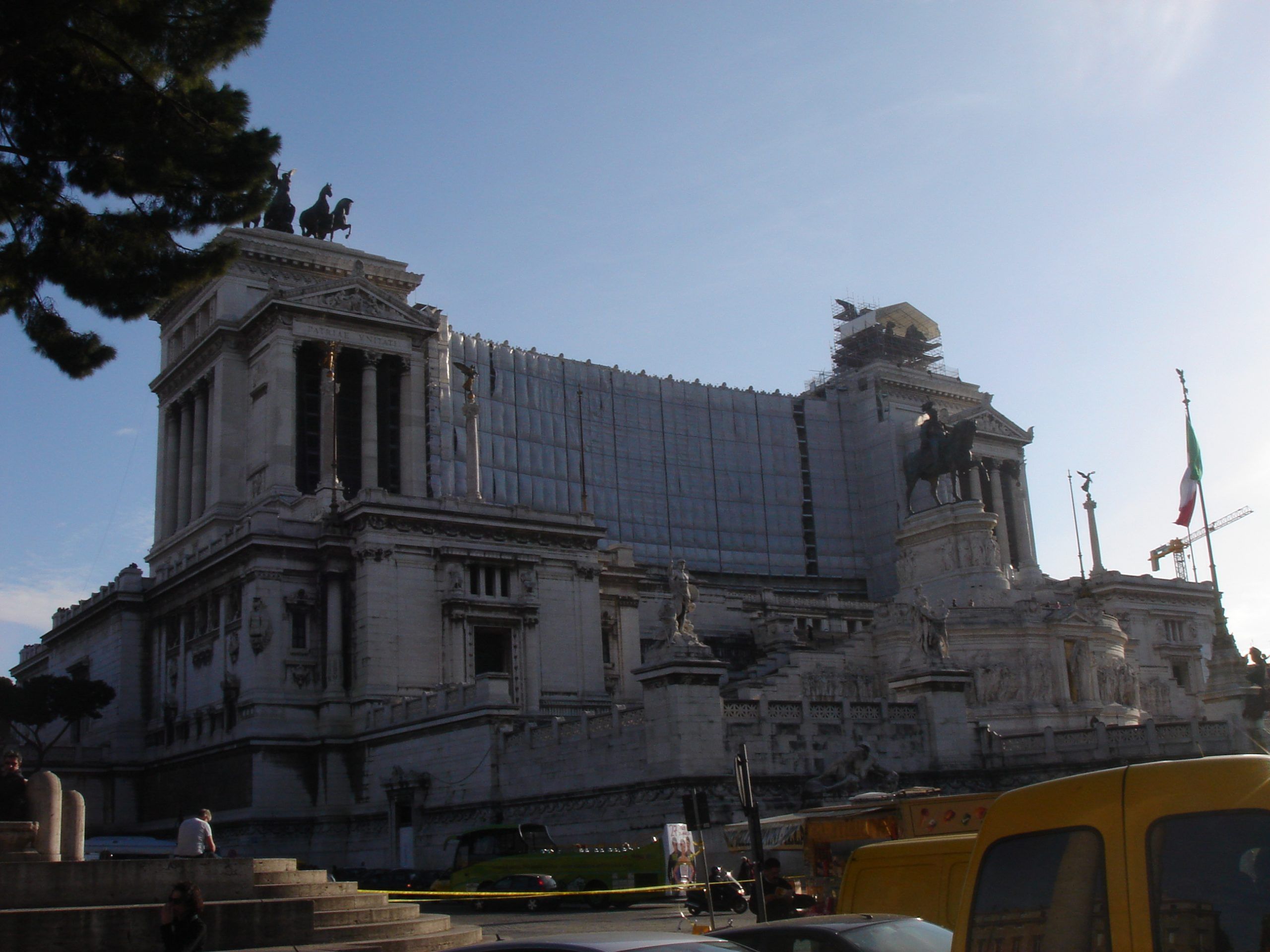 The grand white marble monument to Vittorio Emanuele II with equestrian statue and winged chariots, partially covered by scaffolding.
