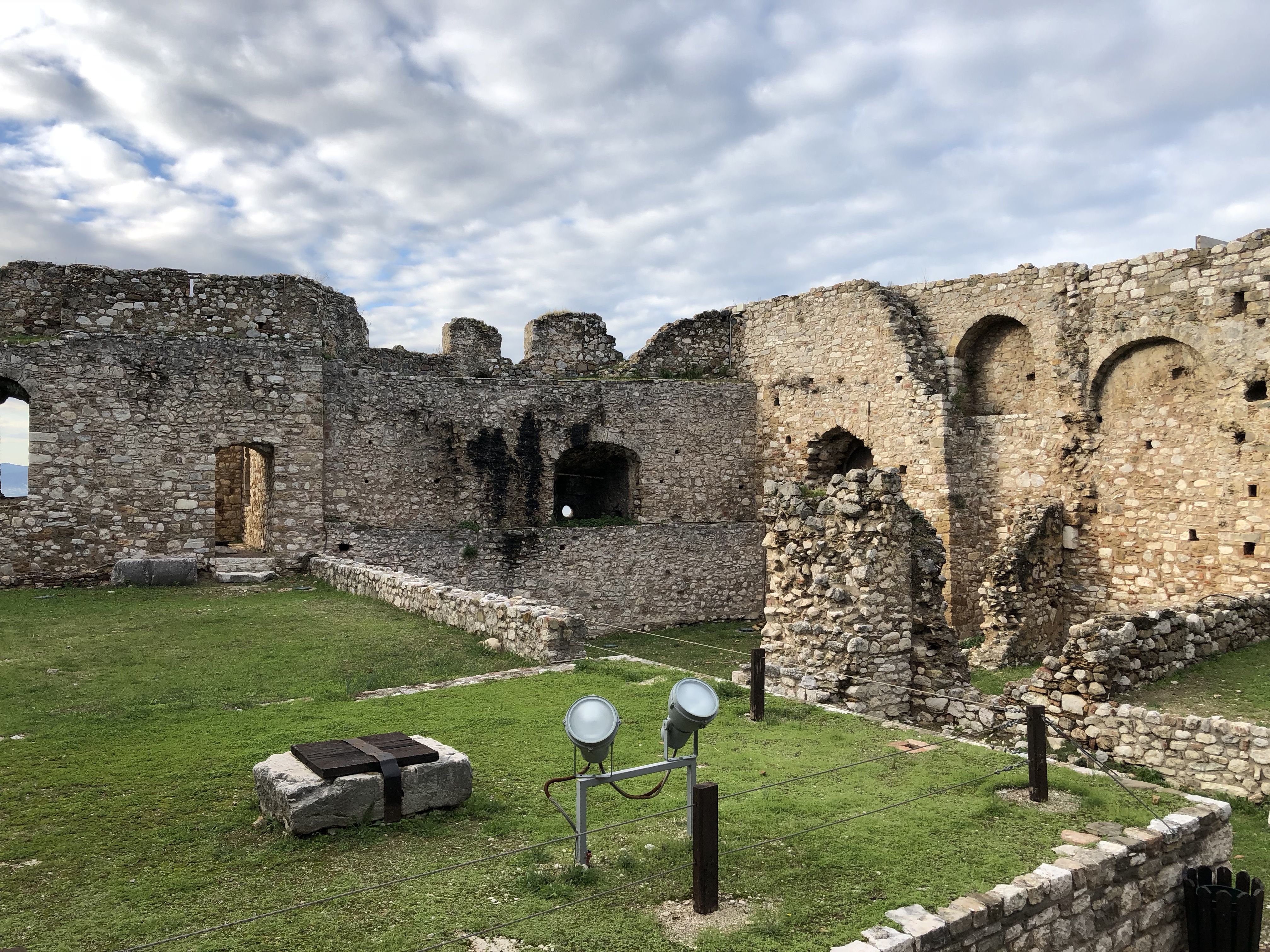Inside the castle again. Remains of a cylindrical structure. The ground is grassy and divided into rectangles by the remains of interior walls.