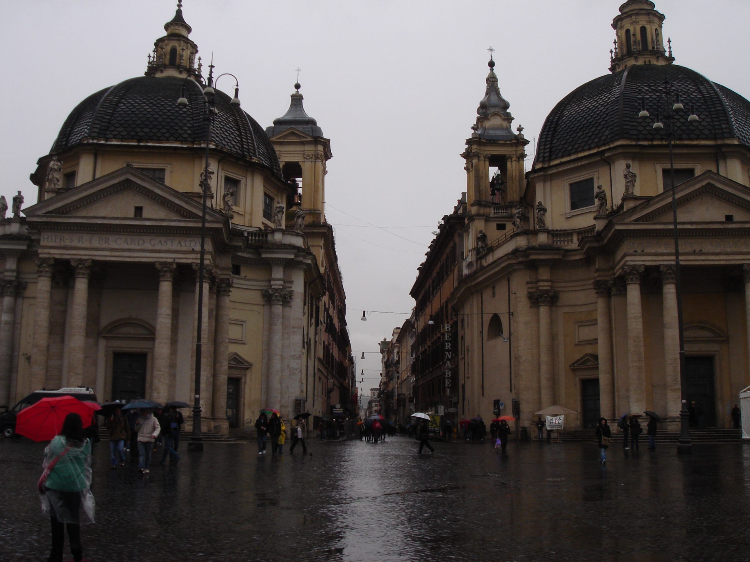 Piazza del Popolo in Rome on a rainy day, with the twin baroque churches of Santa Maria dei Miracoli and Santa Maria in Montesanto flanking the Via del Corso.