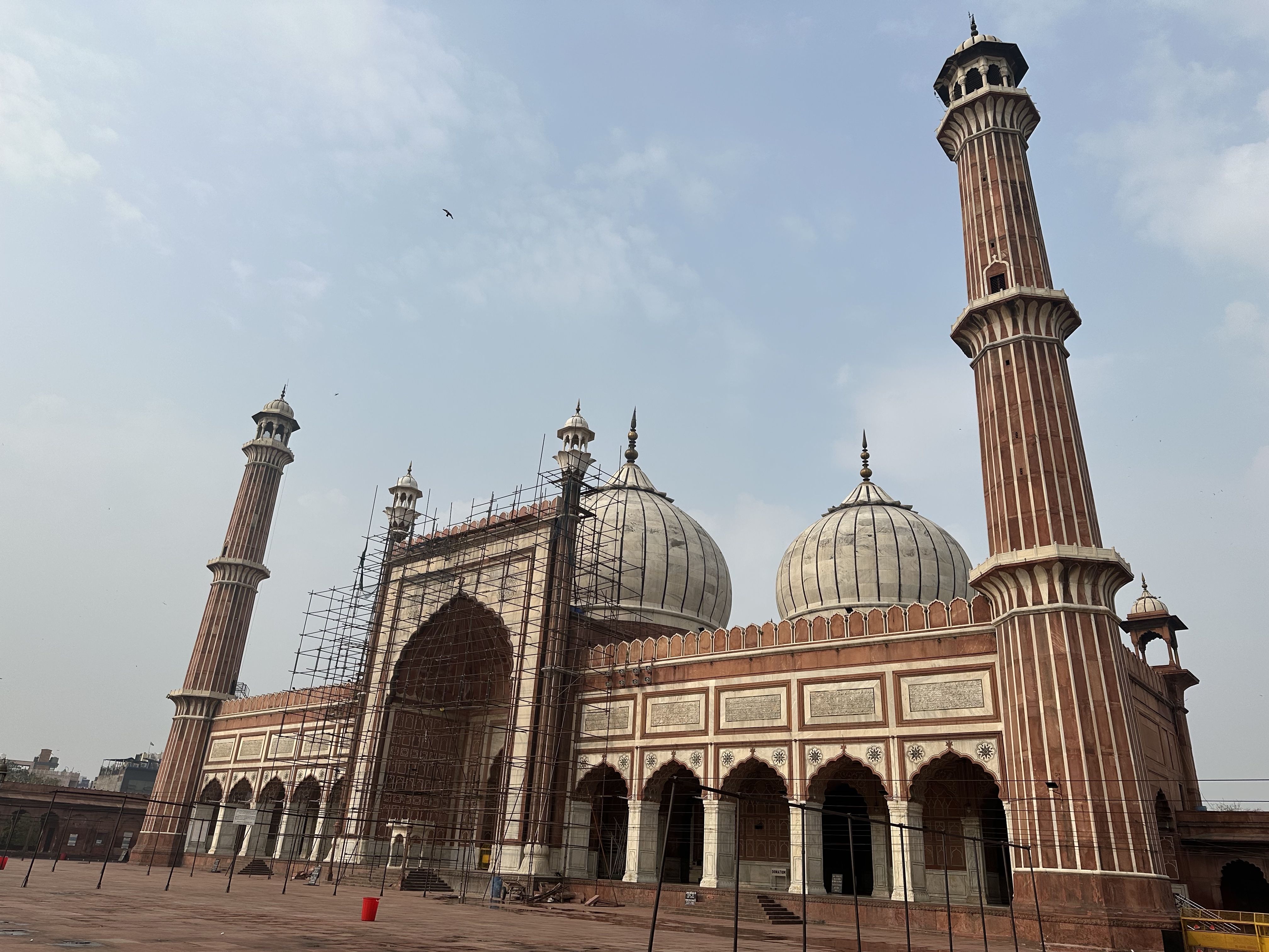 View of Jama Masjid in Delhi, with its domes and minarets partially covered in scaffolding during restoration.