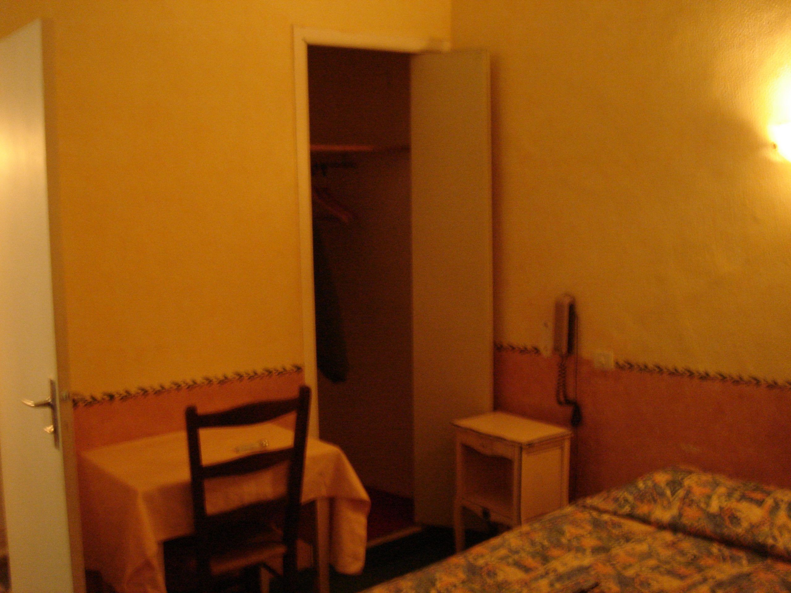 Simple hotel room interior in Nîmes with yellow walls, a small table, and an open closet.